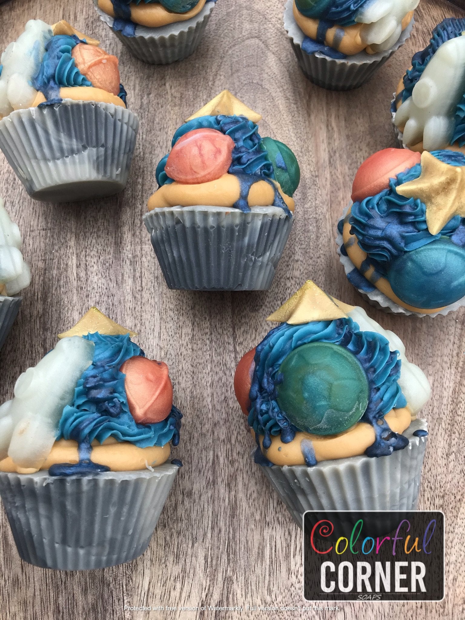 Close up of several soap cupcakes laying on their sides. Displayed several sides to see all the different embeds in the soaps. ( Rocket, star, Earth, and Saturn)