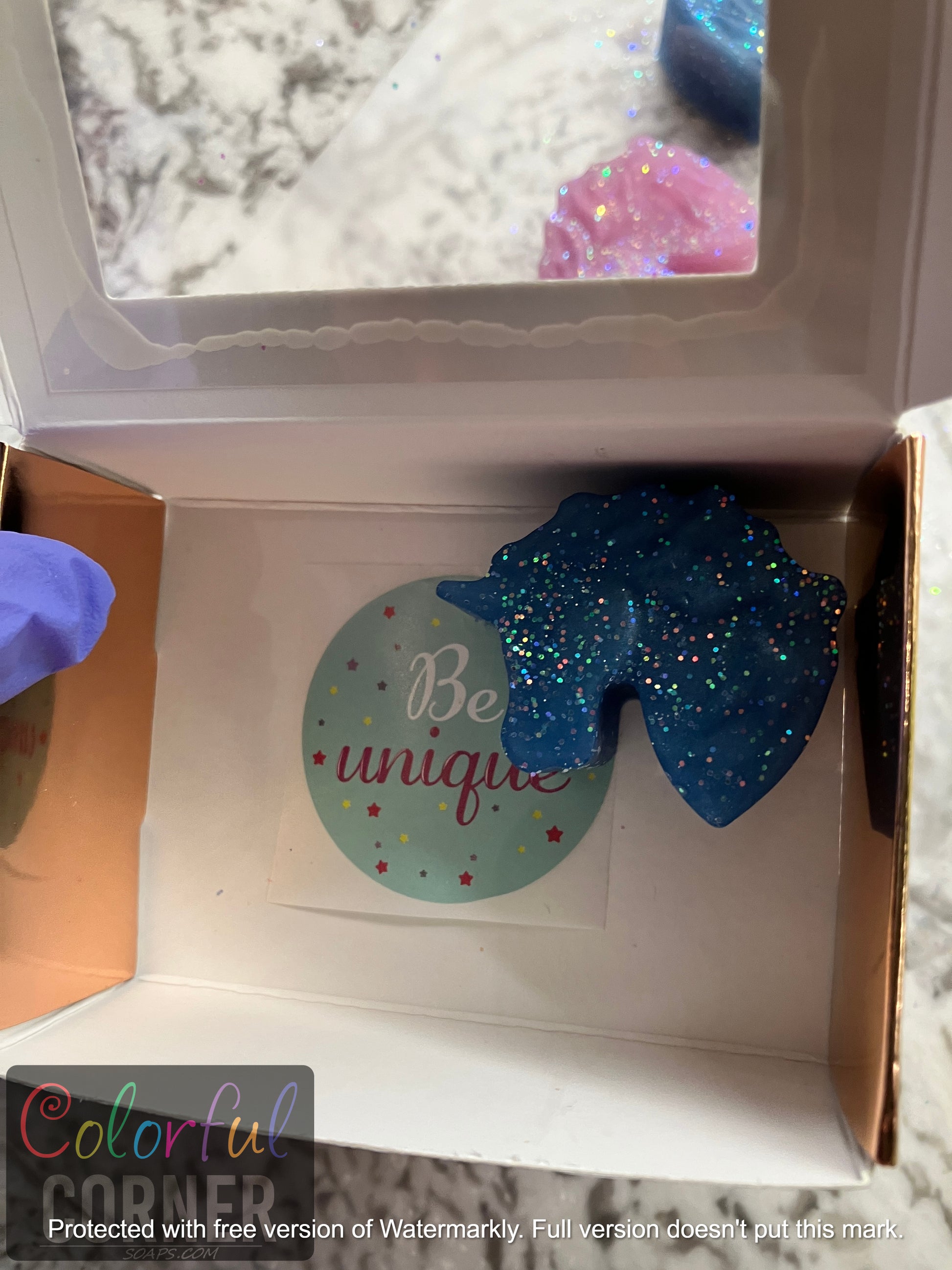 Sicker in the bottom of the package displayed with one blue soap inside the opened rose gold box.