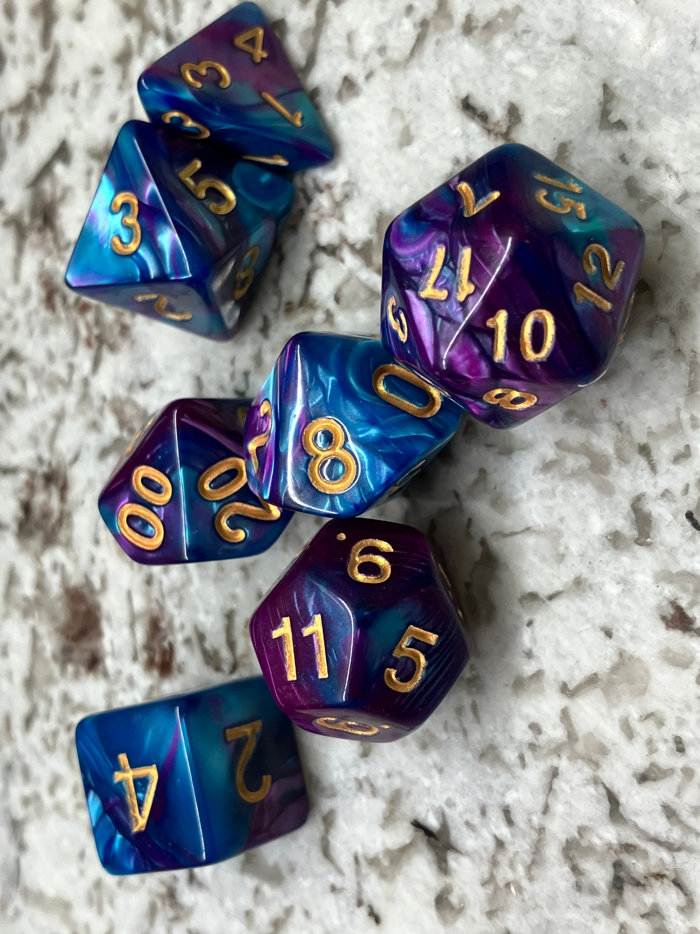 Set of seven dice for role play gaming. Shown in marine blue and dark purple with gold numbering.