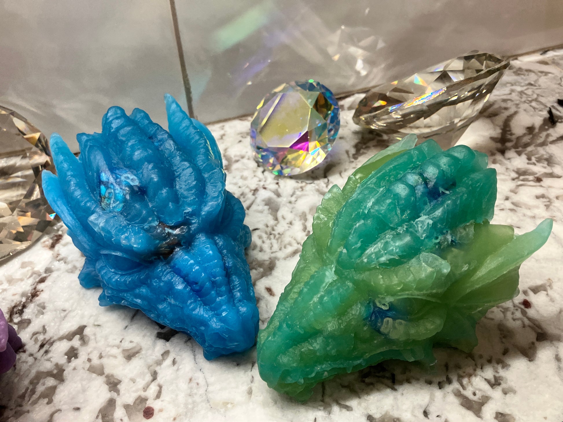 Zoomed in dragon head soaps blue and green shown together with large gems in the background for display only.