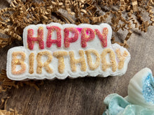 Load image into Gallery viewer, A closeup of a  white &quot;Happy Birthday&quot; bath bomb with balloon-like text. The color of the &quot;Happy&quot; is a grand canyon red with a sparkly gold overlay. The &quot;Birthday&quot; is the same type of sparkly gold as the &quot;Happy&quot; except that the gold there is a solid color. 
