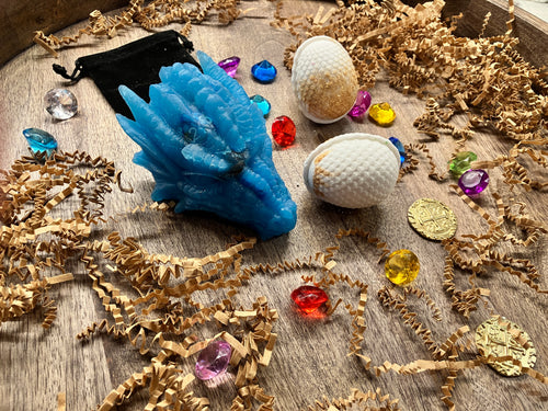 Tray full of treasures displayed. Included in the photo are the small velvet bag included, the large blue dragon head soap with dice inside, two dragon egg bath bombs, two 'golden toned' play coins, and 15 'gems' for fun.